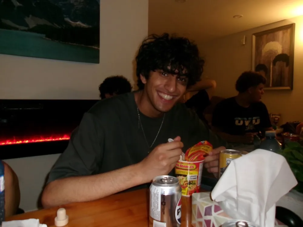 Shaan grinning over a cup of instant noodles at a table of friends