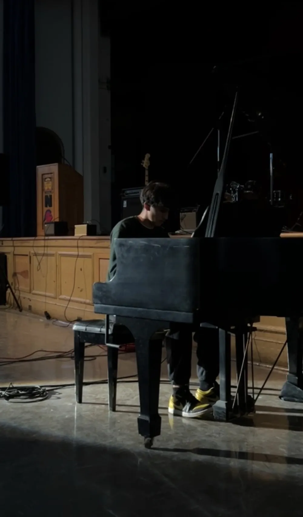 Shaan at a grand piano on a darkened stage